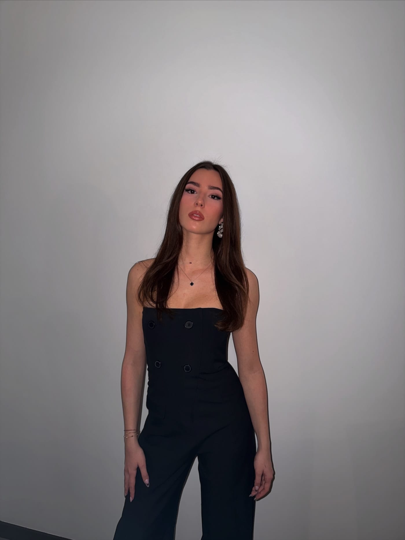 Ena Meleh in a black jumpsuit against a plain studio wall